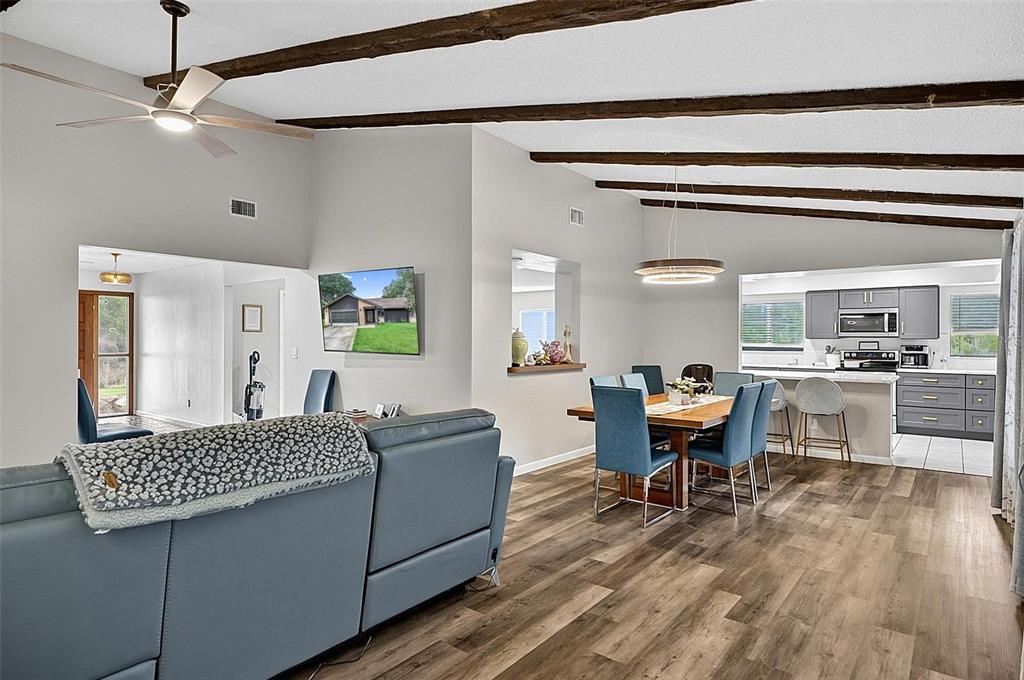 An open-concept living and dining area features wood-look flooring, exposed ceiling beams, and gray cabinetry — 3 BLAKE COURT, PALM COAST, FL
