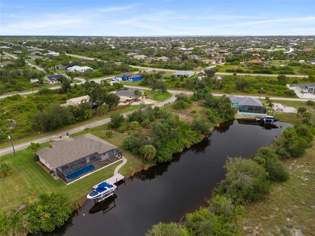 An aerial view shows two waterfront houses with screened pools and boat docks on a canal — 13902 BEGONIA CIRCLE, PORT CHARLOTTE, FL