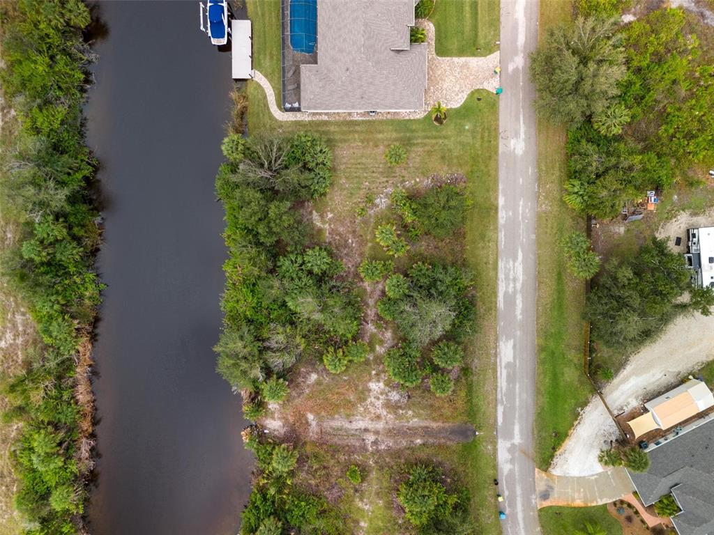An aerial view shows a vacant, wooded residential lot situated between a canal and a road — 13902 BEGONIA CIRCLE, PORT CHARLOTTE, FL