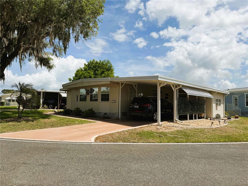 A single-story mobile home with a carport and a paved driveway under a blue sky — 121 AZALEA TRAIL, LEESBURG, FL