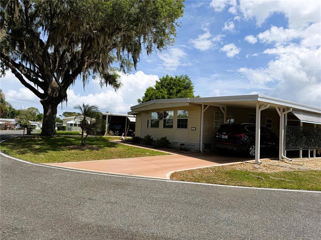 A single-story manufactured home with a carport and a large oak tree in front — 121 AZALEA TRAIL, LEESBURG, FL