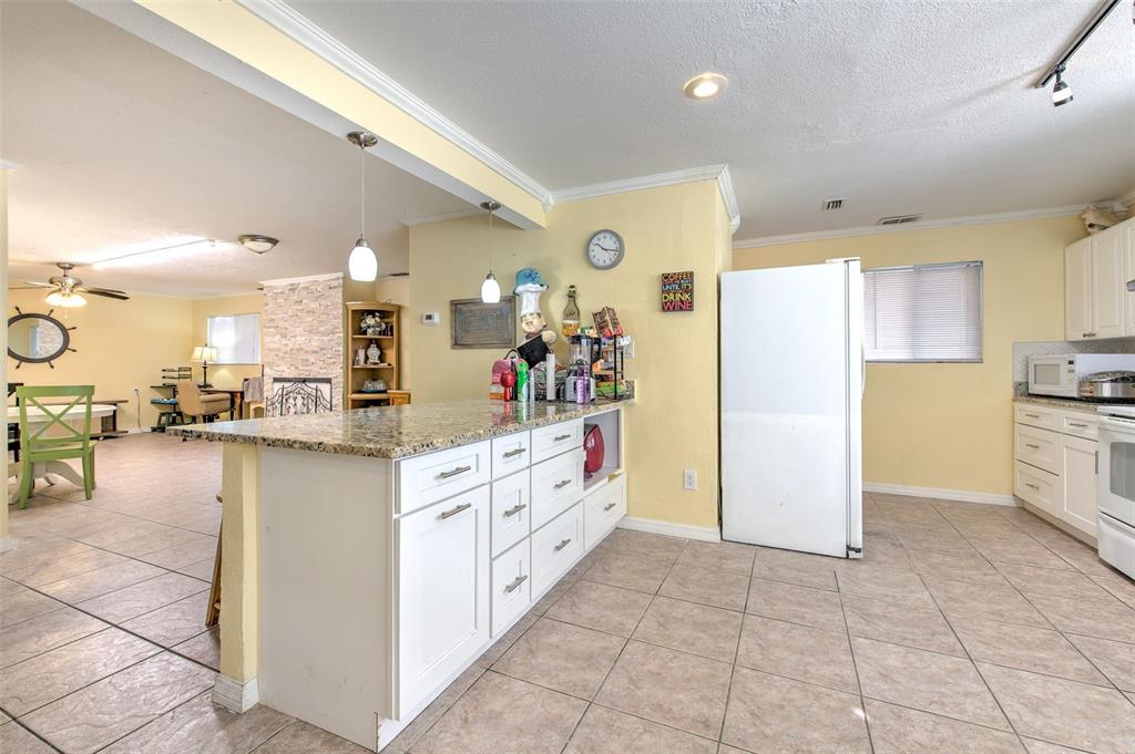 A kitchen with white cabinets, granite countertops, and tile flooring opens into a living area — 5415 MILES BOULEVARD, PORT RICHEY, FL