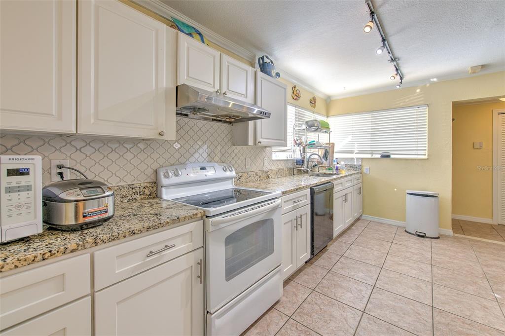 A kitchen features white cabinets, granite countertops, a tiled backsplash, and stainless steel appliances — 5415 MILES BOULEVARD, PORT RICHEY, FL