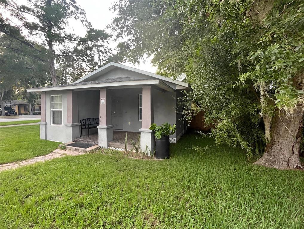 A small, gray, single-story house with a covered front porch and a large oak tree — 1712 W MAIN STREET, LEESBURG, FL