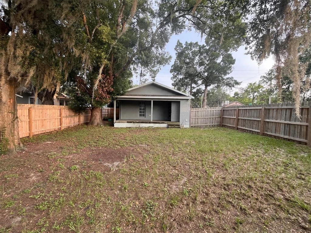 A backyard view of a small house with a covered porch and a wooden fence — 1712 W MAIN STREET, LEESBURG, FL