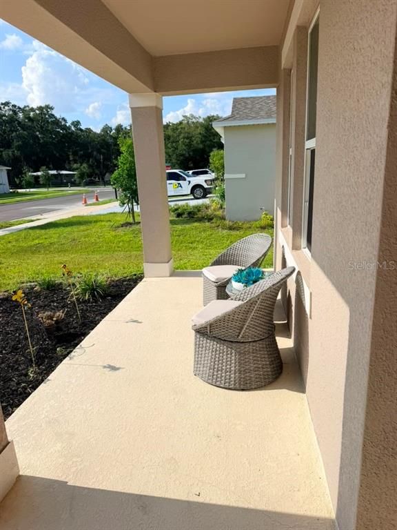 A covered porch features two wicker chairs and a small table overlooking a residential street — 1383 LEVY BEND DRIVE, KISSIMMEE, FL