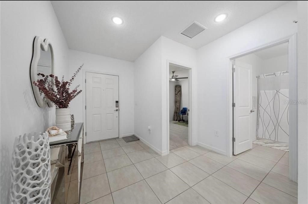 A bright entryway with light tile flooring, a white front door, and two interior doorways — 1383 LEVY BEND DRIVE, KISSIMMEE, FL