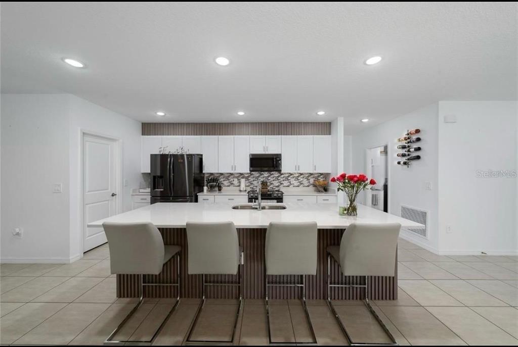 A modern kitchen features a large white island, four gray chairs, and white cabinetry — 1383 LEVY BEND DRIVE, KISSIMMEE, FL