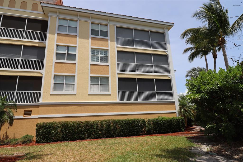 A multi-story yellow stucco building features screened-in balconies and a manicured hedge in front — 255 W END DRIVE UNIT 2210, PUNTA GORDA, FL
