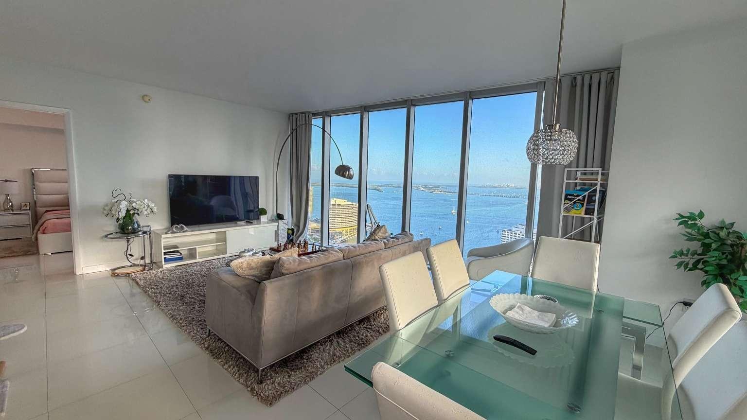 A modern living and dining area features floor-to-ceiling windows with a view of the water — 485 Brickell Avenue # 3608, Miami FL 33131, MIAMI, FL