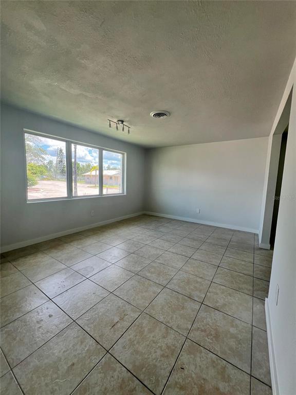 An empty room features light-colored tile flooring, white walls, and a large window — 744 LEMON AVENUE, SEBRING, FL