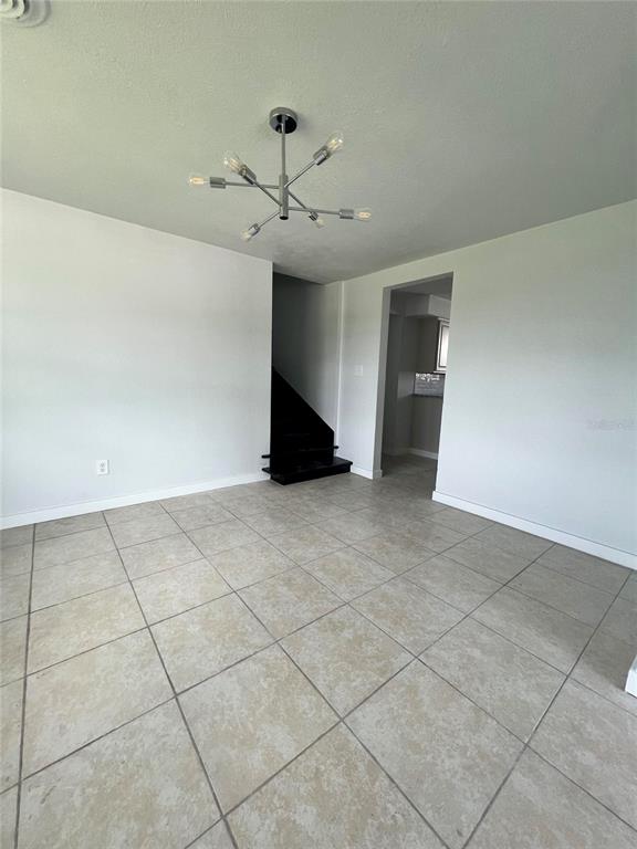 A room with light-colored tile flooring, a modern chandelier, and a black staircase — 744 LEMON AVENUE, SEBRING, FL