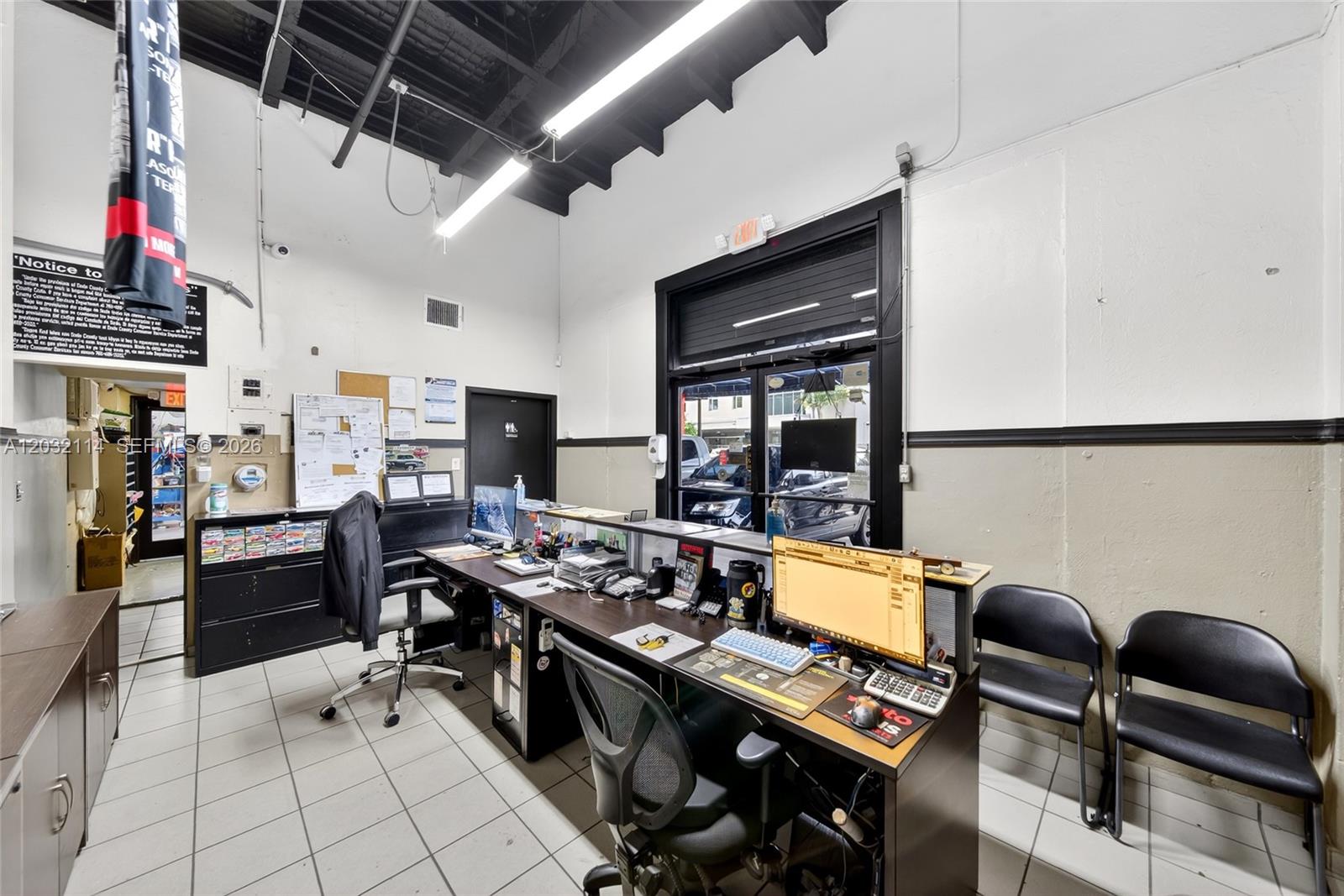 An office interior features a long desk, computer equipment, tiled flooring, and high ceilings — MIAMI, FL