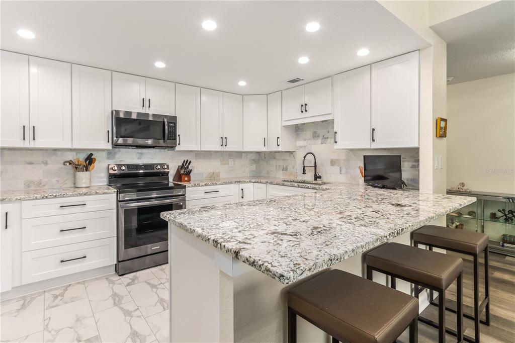 A white kitchen features granite countertops, stainless steel appliances, and a breakfast bar with stools — 4 BELLEVIEW BOULEVARD UNIT 205, CLEARWATER, FL