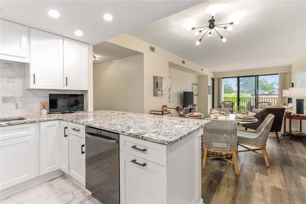 A kitchen with white cabinets and granite countertops overlooks a dining area and living room — 4 BELLEVIEW BOULEVARD UNIT 205, CLEARWATER, FL