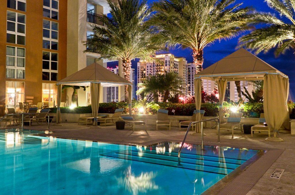 A swimming pool with lounge chairs and cabanas sits outside a multi-story building at night — 550 Okeechobee Boulevard # 604, West Palm Beach FL 33401, WEST PALM BEACH, FL