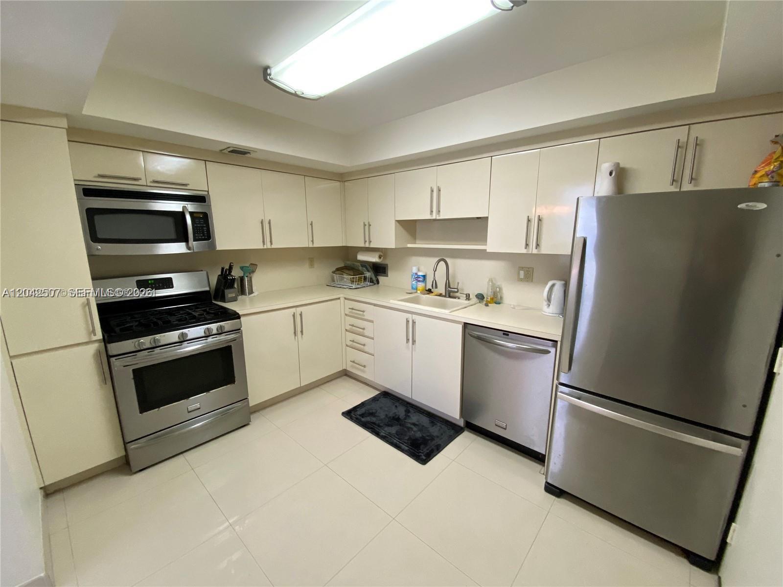 A kitchen features off-white cabinets, stainless steel appliances, and light-colored tile flooring — 2030 S Ocean Dr # 412, Hallandale Beach FL 33009, HALLANDALE BEACH, FL