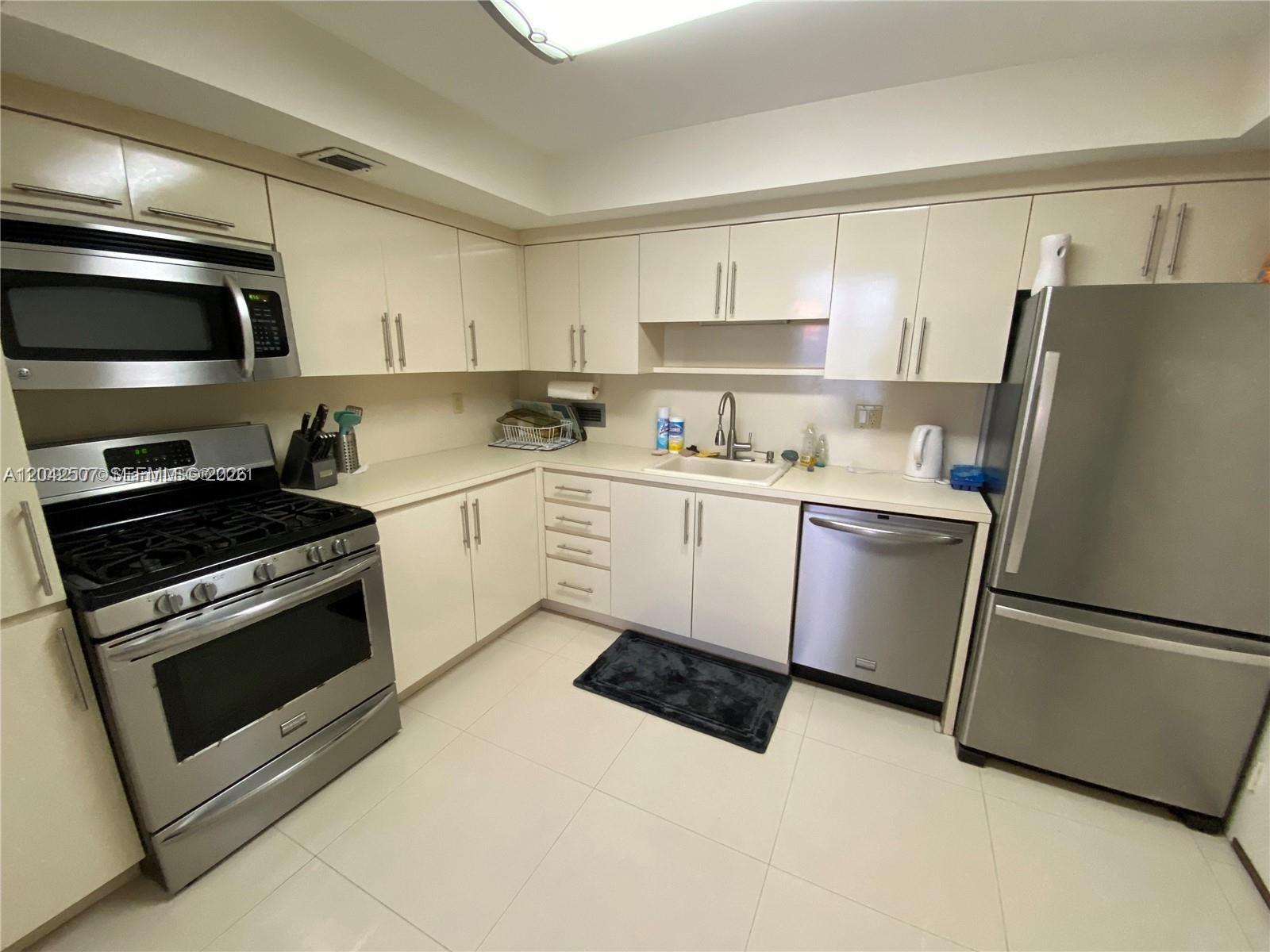 A kitchen features off-white cabinets, stainless steel appliances, and light-colored tile flooring — 2030 S Ocean Dr # 412, Hallandale Beach FL 33009, HALLANDALE BEACH, FL