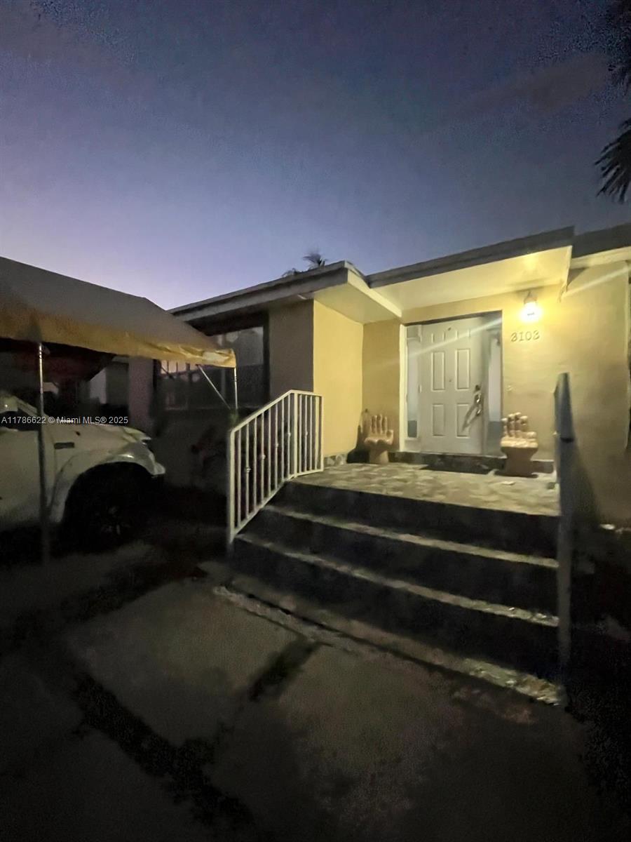 The exterior of a house at dusk features a front porch with stairs and railings — 3103 NW 157th St, Miami Gardens FL 33054, MIAMI GARDENS, FL