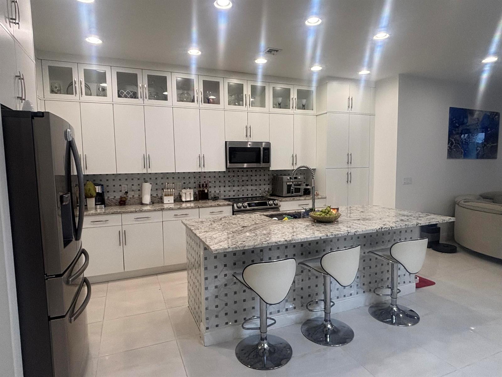 A modern kitchen features white cabinetry, granite countertops, a tiled island, and stainless steel appliances — 4834 Sand Dollar Drive, Westlake FL 33470, WESTLAKE, FL
