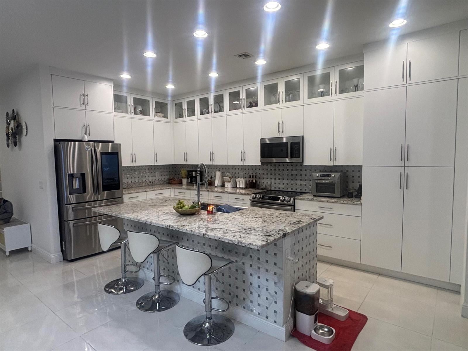 A modern kitchen features white cabinetry, granite countertops, a central island, and stainless steel appliances — 4834 Sand Dollar Drive, Westlake FL 33470, WESTLAKE, FL