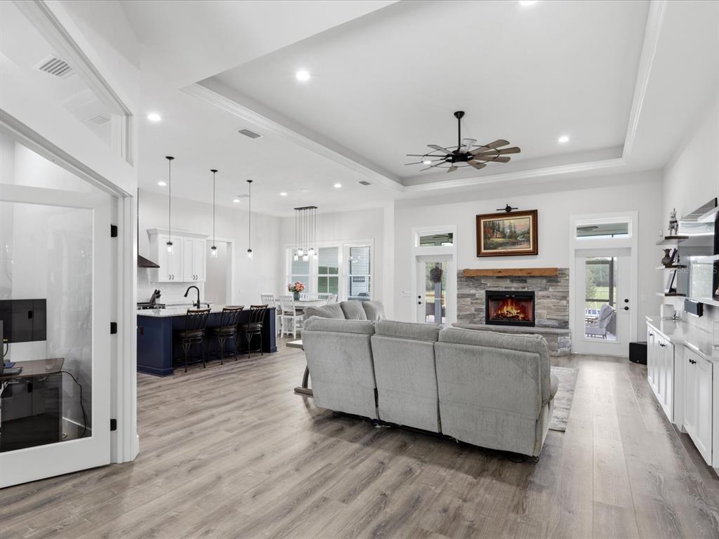 An open-concept living room and kitchen featuring a stone fireplace, gray sofa, and wood flooring — 7311 NW 218TH STREET, ALACHUA, FL