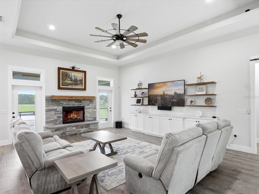 A living room features a stone fireplace, white cabinetry, floating shelves, and a tray ceiling — 7311 NW 218TH STREET, ALACHUA, FL