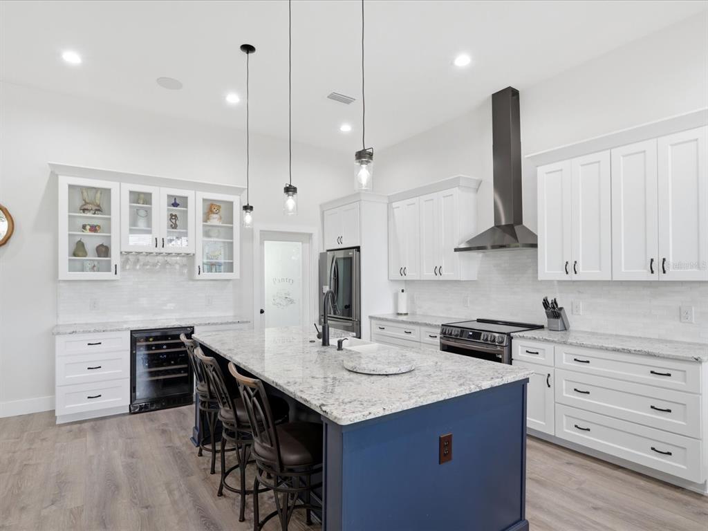 A modern kitchen features white cabinetry, a blue island with bar seating, and granite countertops — 7311 NW 218TH STREET, ALACHUA, FL