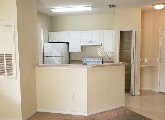 A kitchen with white cabinets, white appliances, and a breakfast bar overlooking a carpeted area — 18001 RICHMOND PLACE DRIVE UNIT 525, TAMPA, FL