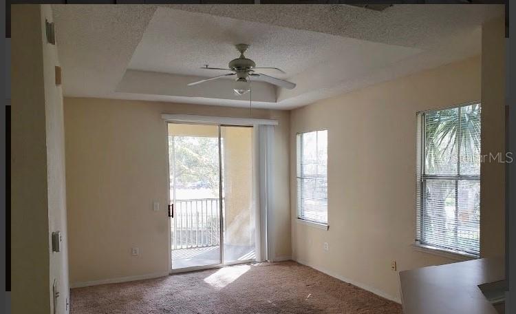 A living room with beige walls, carpeted flooring, a ceiling fan, and a sliding glass door — 18001 RICHMOND PLACE DRIVE UNIT 525, TAMPA, FL