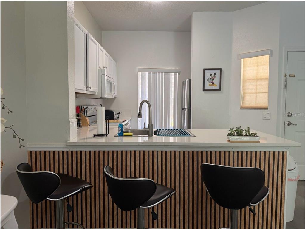A kitchen features white cabinets, a breakfast bar with wood-slat paneling, and three bar stools — 1119 PARK RIDGE CIRCLE, KISSIMMEE, FL