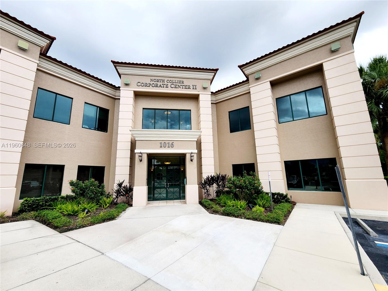 The exterior of a two-story commercial building with a beige facade and green-tinted windows — 1016 Collier Center Way # 106, Naples FL 34110, NAPLES, FL