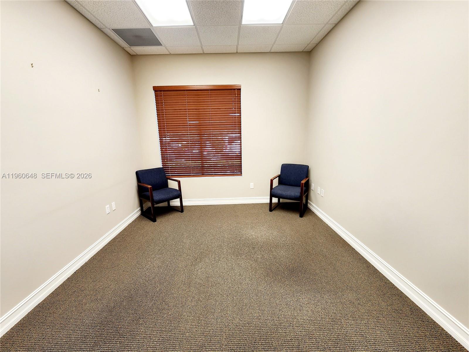 An empty office room features beige walls, brown carpet, and two dark blue armchairs — 1016 Collier Center Way # 106, Naples FL 34110, NAPLES, FL