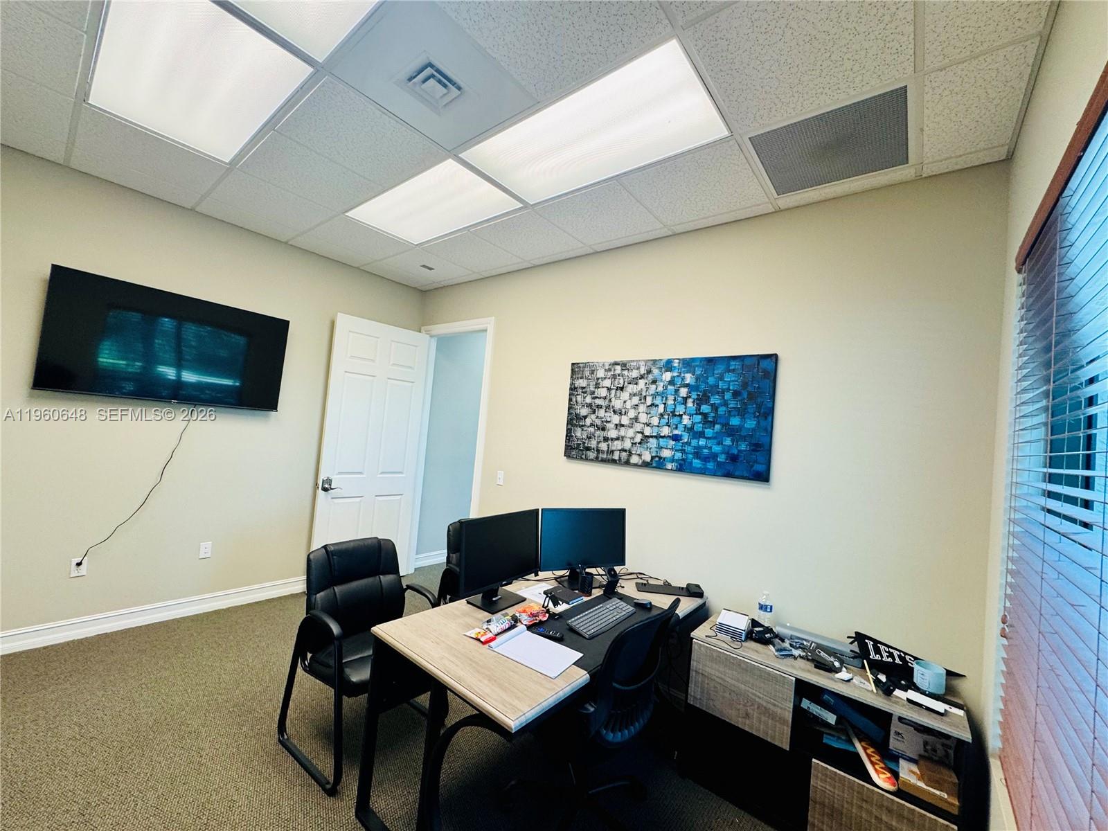 An office space features a desk with dual monitors, a wall-mounted television, and abstract art — 1016 Collier Center Way # 106, Naples FL 34110, NAPLES, FL