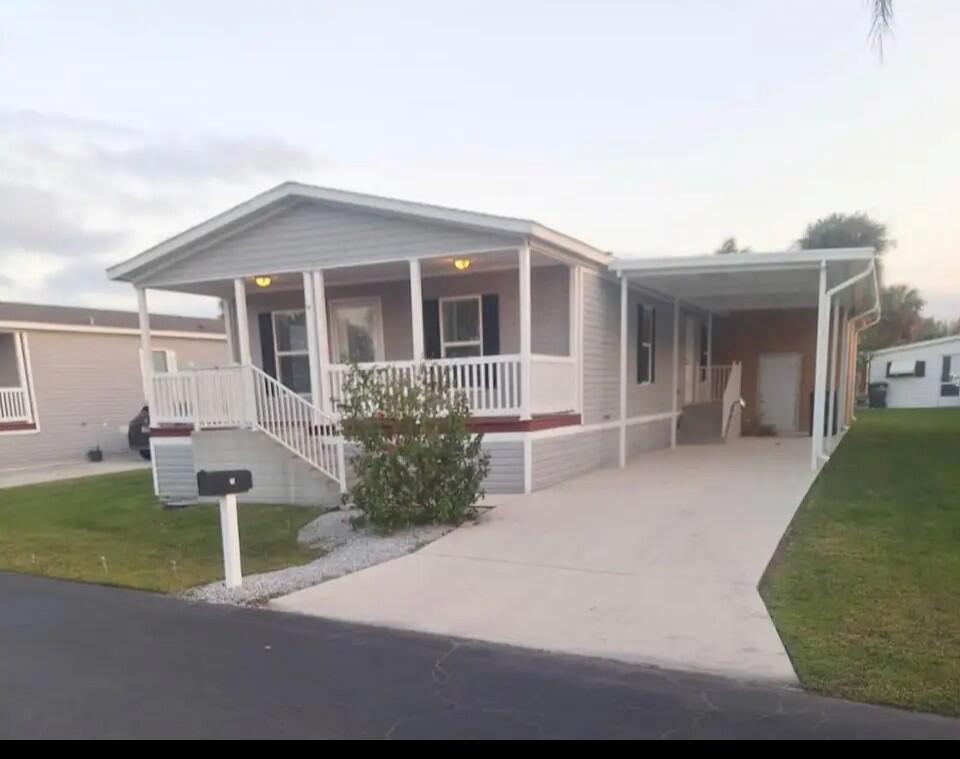 A single-story manufactured home with a front porch, concrete driveway, and attached carport — 76 Sandhill Boulevard, Fort Pierce FL 34982, FORT PIERCE, FL
