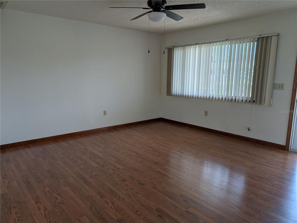 An empty room features hardwood flooring, white walls, a ceiling fan, and vertical window blinds — 10881 SW 78TH COURT, OCALA, FL