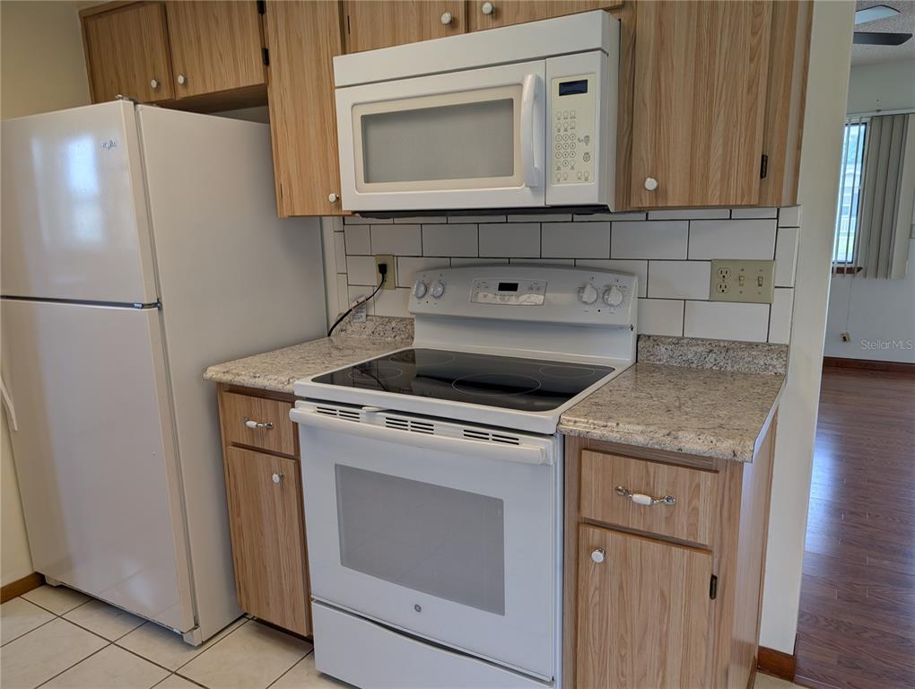 A kitchen features white appliances, wood cabinets, granite countertops, and a white subway tile backsplash — 10881 SW 78TH COURT, OCALA, FL