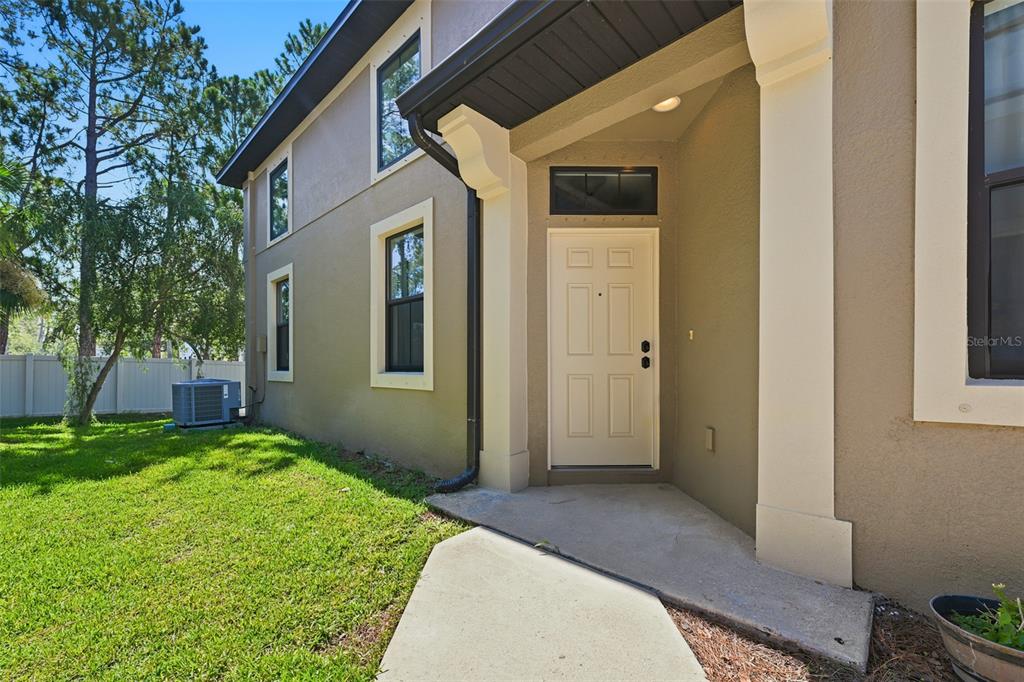 A side view of a house exterior shows a beige door, windows, and a lawn — 5156 BAY ISLE CIRCLE, CLEARWATER, FL