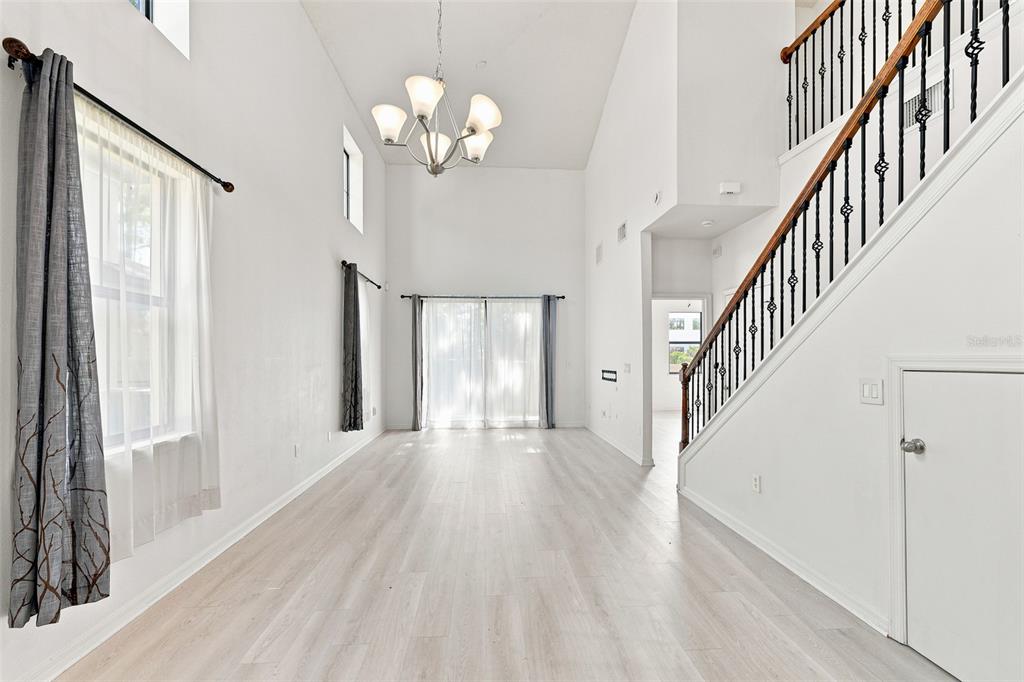 A bright, high-ceilinged living area features light wood-look flooring, a chandelier, and a staircase — 5156 BAY ISLE CIRCLE, CLEARWATER, FL