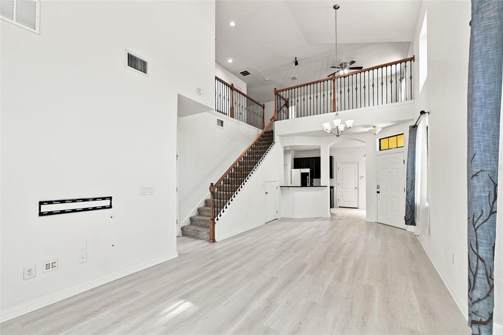 A bright, open-concept living room features high ceilings, a staircase, and light wood-look flooring — 5156 BAY ISLE CIRCLE, CLEARWATER, FL