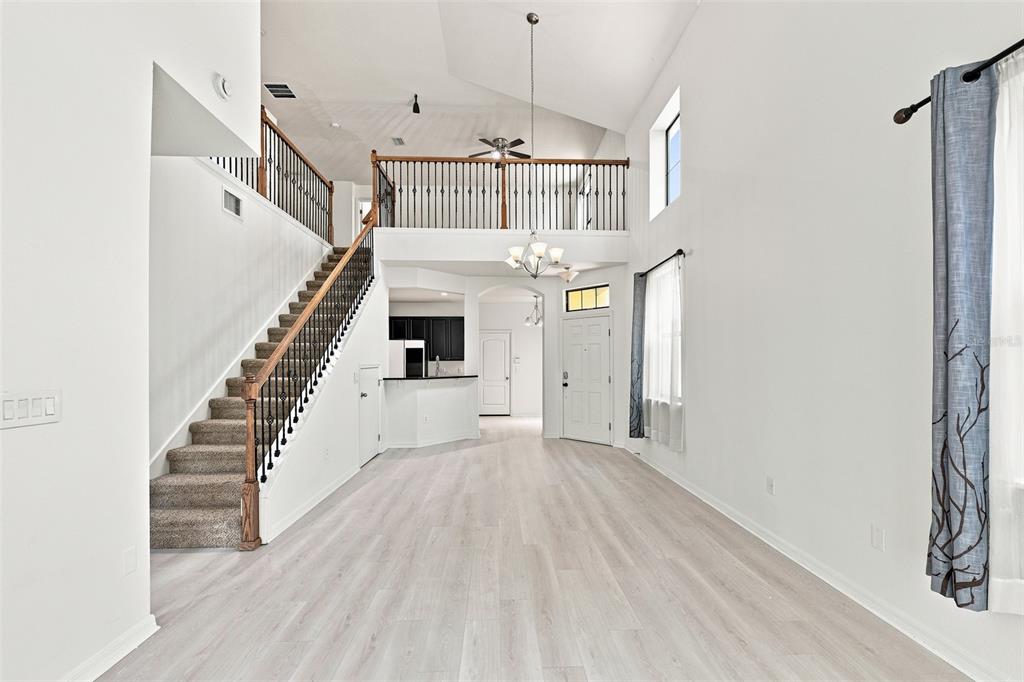 A bright, open-concept living area features a high ceiling, carpeted staircase, and a loft overlook — 5156 BAY ISLE CIRCLE, CLEARWATER, FL