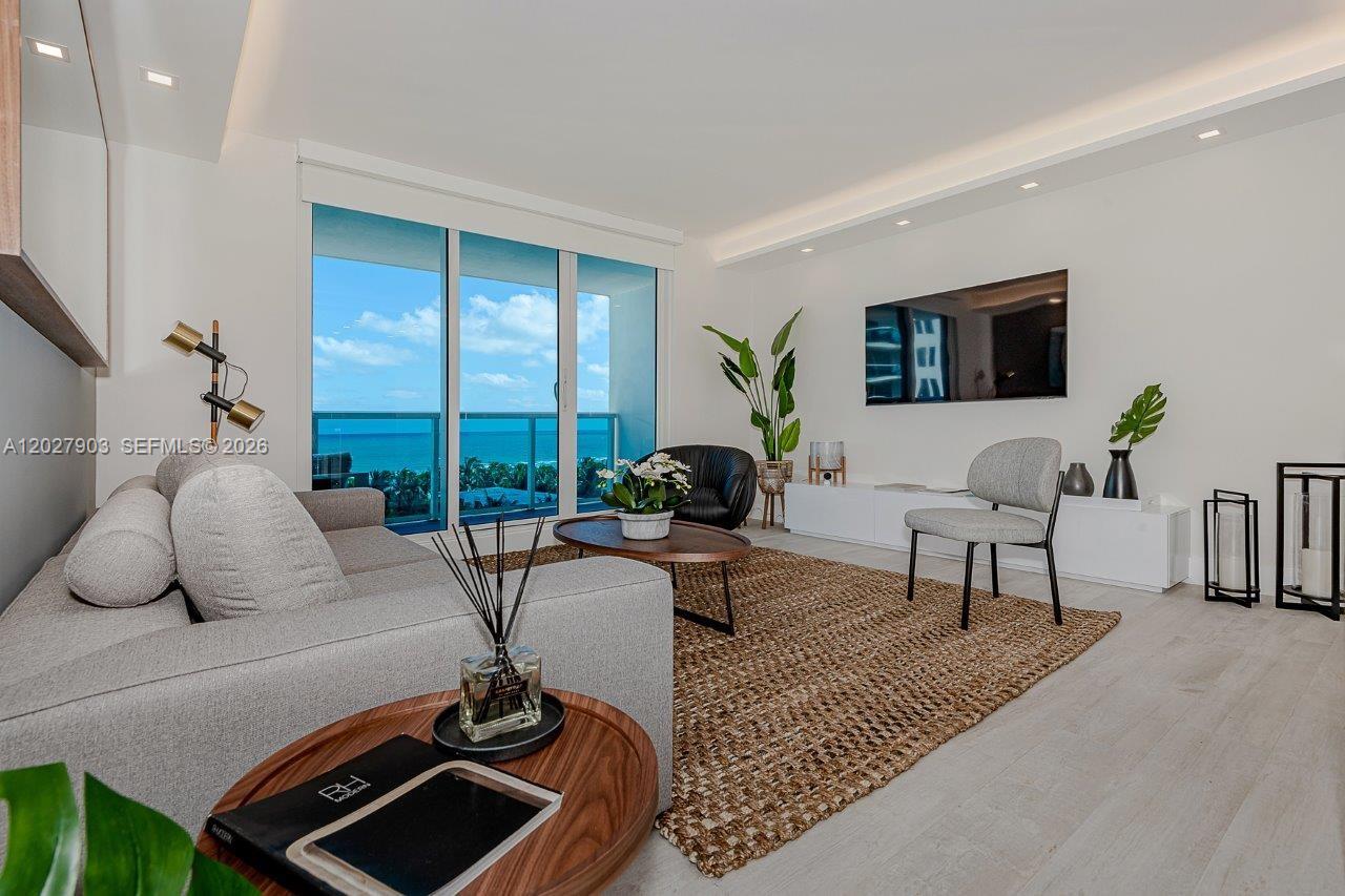 A modern living room features a grey sofa, a textured rug, and a balcony view — 2301 Collins Ave # 739, Miami Beach FL 33139, MIAMI BEACH, FL
