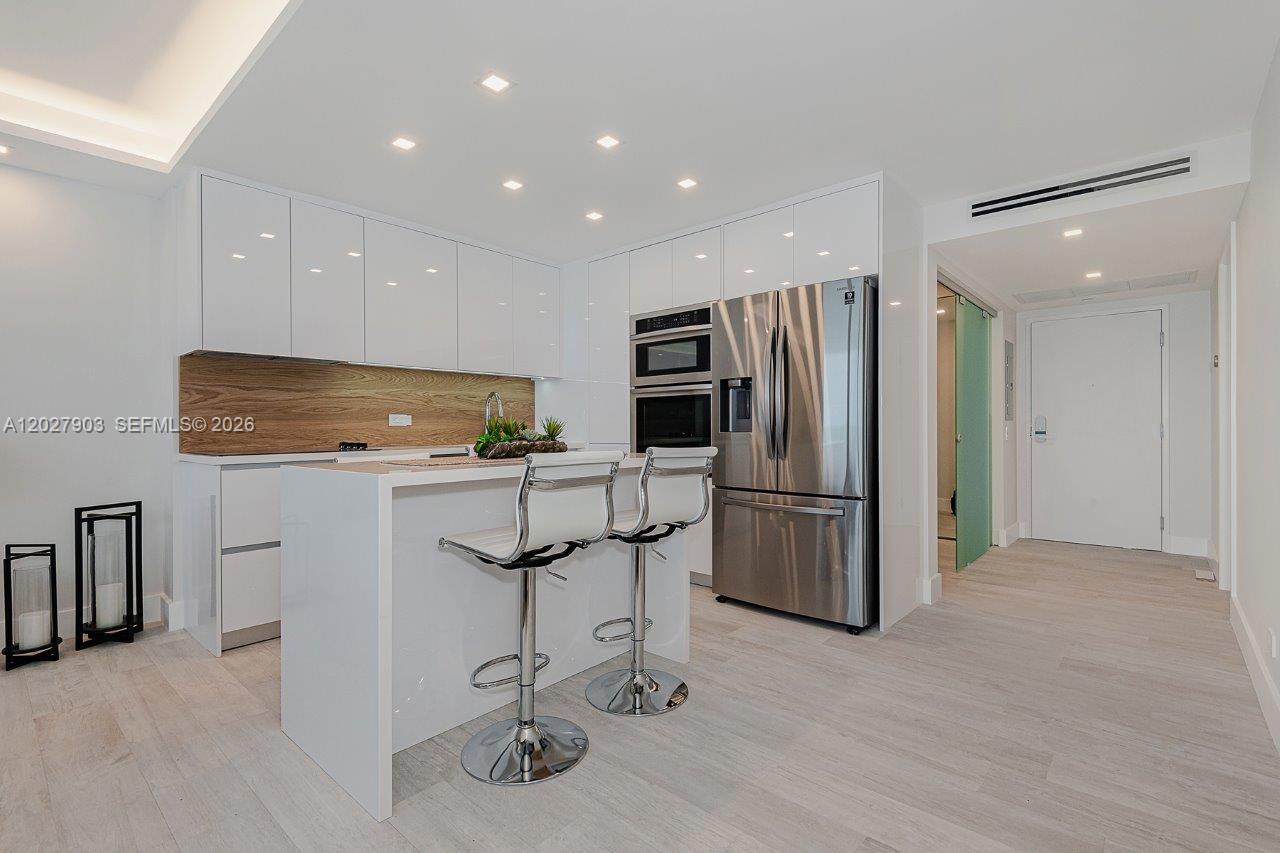 A modern white kitchen features a central island with bar stools and stainless steel appliances — 2301 Collins Ave # 739, Miami Beach FL 33139, MIAMI BEACH, FL
