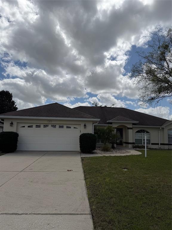 A single-story house with a two-car garage, beige stucco exterior, and a dark shingled roof — 4572 NW 32ND STREET, OCALA, FL
