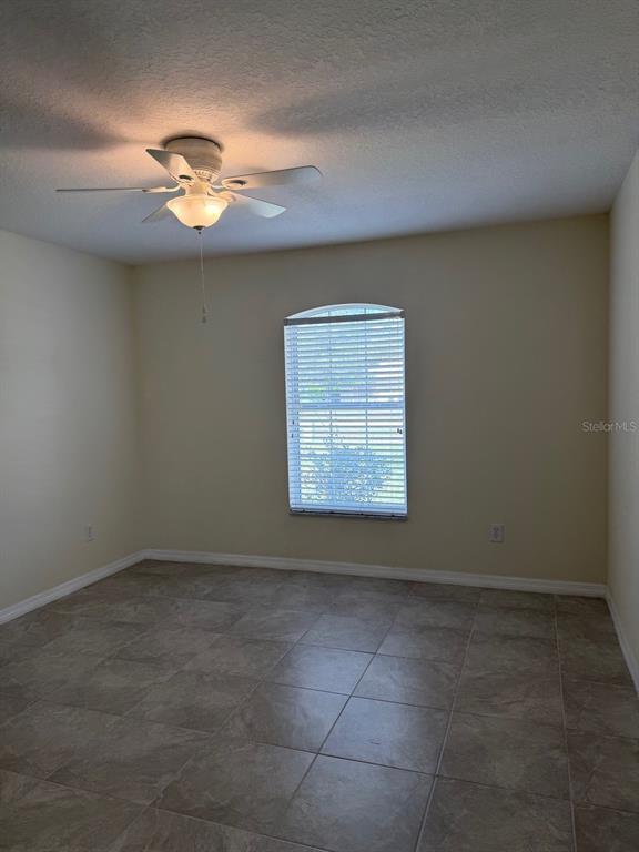 An empty room with beige walls, tile flooring, a ceiling fan, and an arched window — 4572 NW 32ND STREET, OCALA, FL