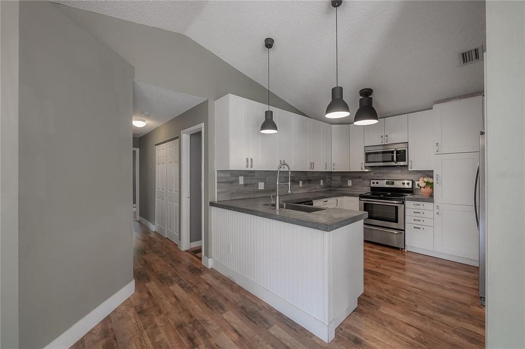 A kitchen features white cabinetry, a gray wood-look backsplash, and a peninsula with gray countertops — 2756 BRAHAM COURT, PALM HARBOR, FL