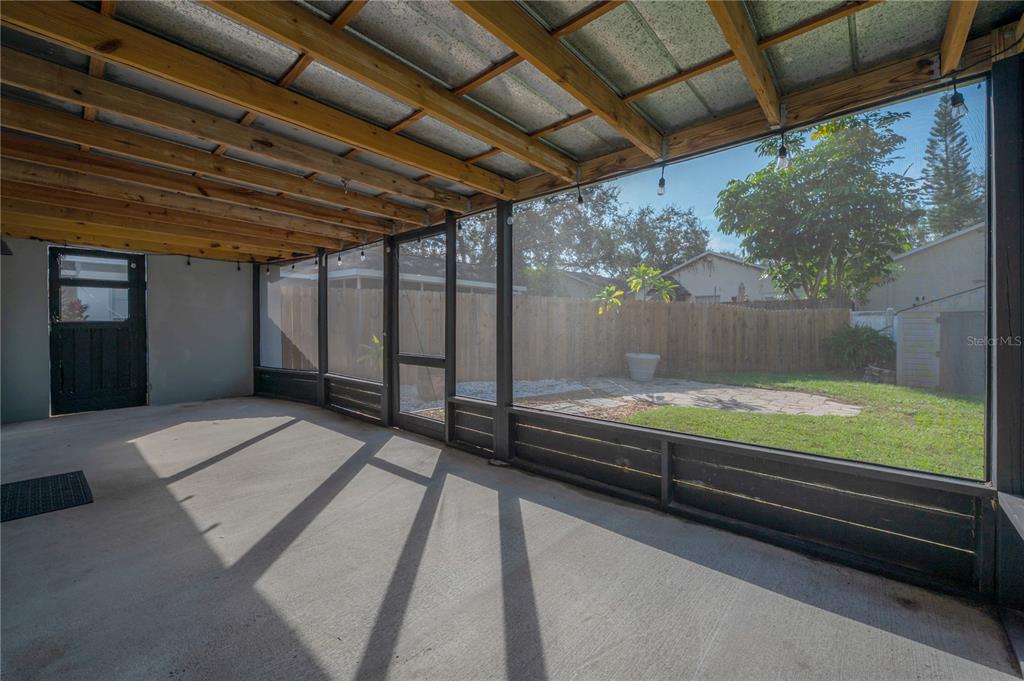 A screened-in patio with a concrete floor, exposed wood ceiling beams, and a fenced backyard — 2756 BRAHAM COURT, PALM HARBOR, FL
