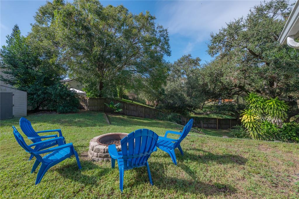 A backyard features a stone fire pit surrounded by three blue Adirondack chairs on grass — 2756 BRAHAM COURT, PALM HARBOR, FL