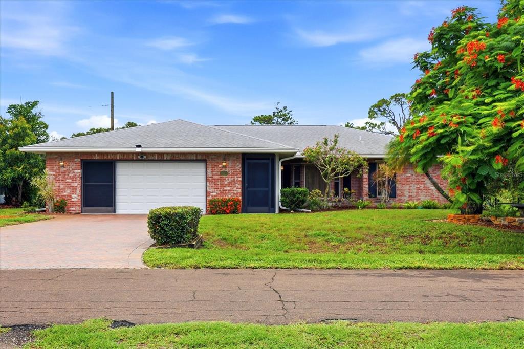 A single-story brick house with a white garage door and a large flowering tree — 1175 CAPLES STREET, ENGLEWOOD, FL