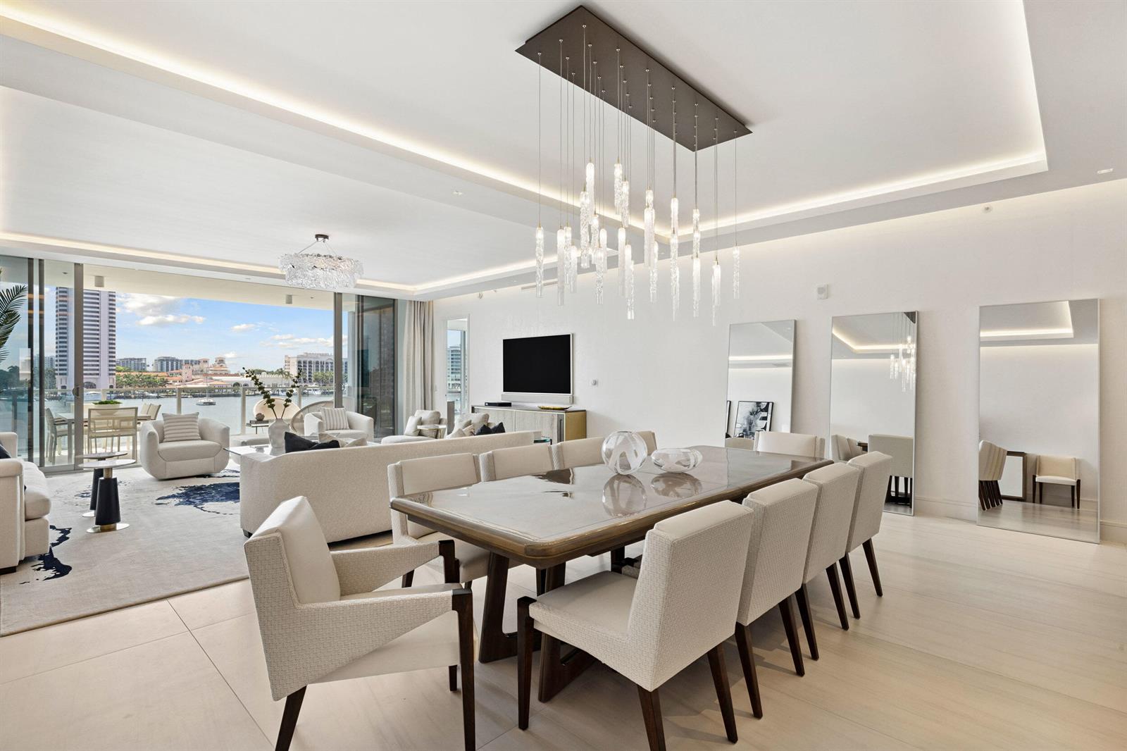 A modern dining and living area features a glass table, crystal chandelier, and balcony view — 725 S Ocean Boulevard # 402, Boca Raton FL 33432, BOCA RATON, FL